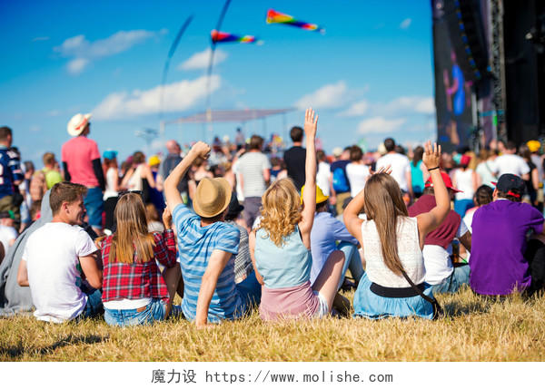 夏季音乐节上一群青少年坐在舞台前的草地上